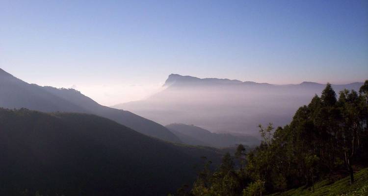 Paysage montagneux brumeux avec une vallée sous un éclairage faible.