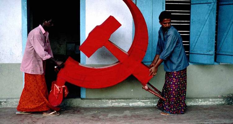 Deux hommes portant un grand symbole communiste rouge dans un environnement intérieur.