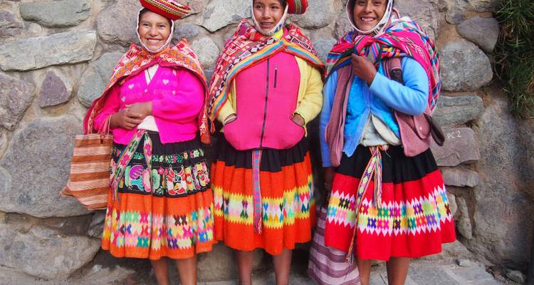 Femmes en tenue traditionnelle posant contre un mur de pierre.