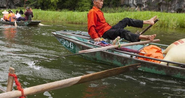 Hombre remando un bote con los pies, turistas en otro bote cerca.