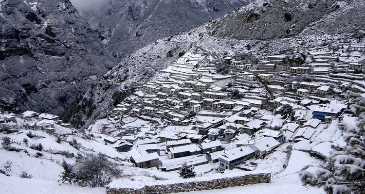 Village enneigé sur une colline avec un arrière-plan montagneux.