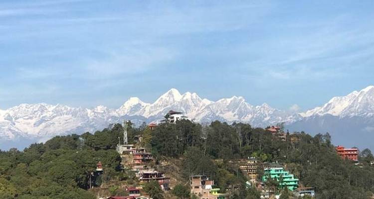 Panoramic view of snow-capped mountains with forests and scattered buildings.