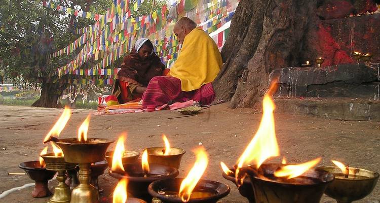 Two people sitting by a tree surrounded by prayer flags and butter lamps.