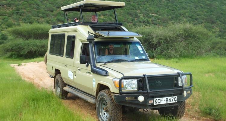 Safari vehicle driving on a dirt road, surrounded by green landscape.