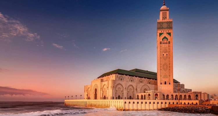 Hassan II Mosque at sunset with ocean waves gently crashing on the shore in Casablanca.