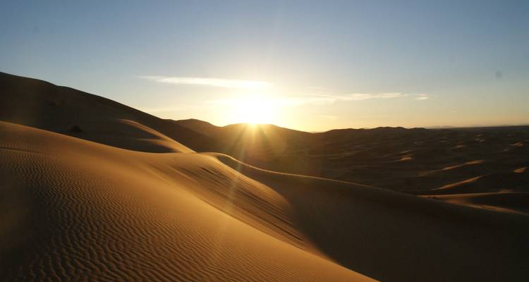 Sand dunes at sunset with the sun near the horizon.