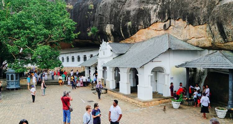 Menschen besuchen einen antiken Tempelkomplex neben einem großen Felsen.