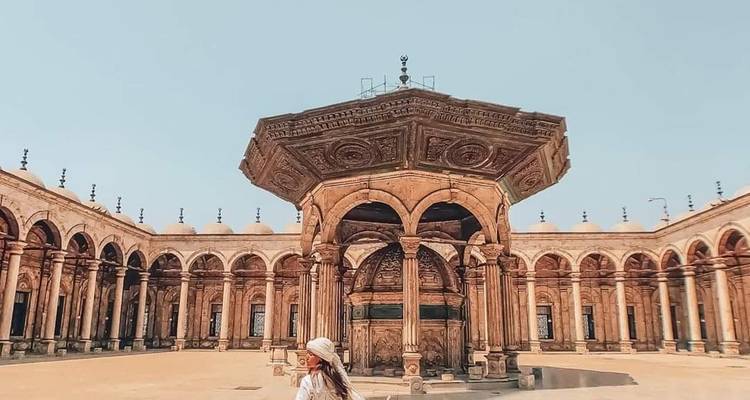 Femme marchant dans une cour historique spacieuse avec une structure ornée.
