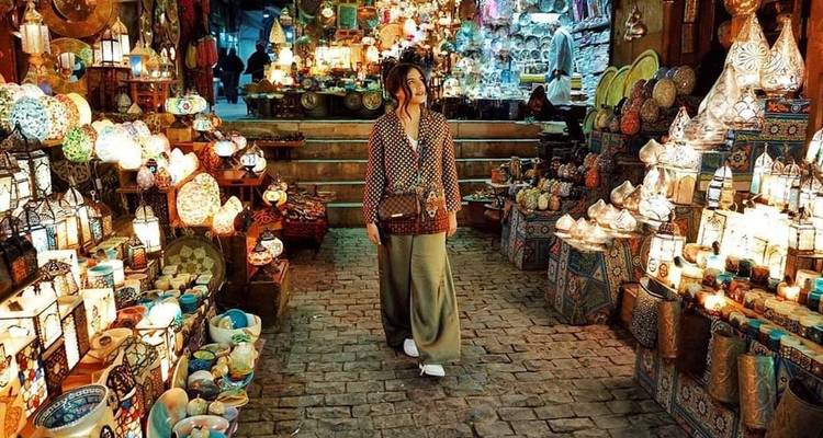 Femme marchant à travers un marché animé rempli de lampes colorées et de décorations.