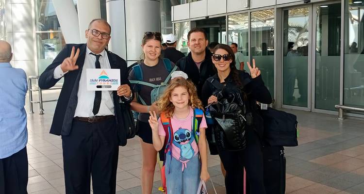 Famille avec bagages dans un terminal d'aéroport tenant une pancarte.