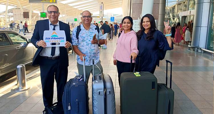 Groupe avec bagages posant dans un aéroport avec un panneau de visite.