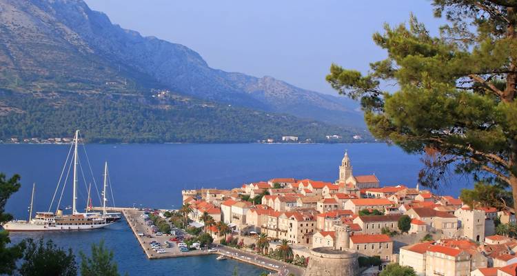 La vieille ville médiévale de Korčula et son port vus d'une colline encadrés par les montagnes et les eaux bleu profond.