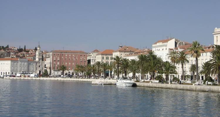 Paseo frente al mar de Split bordado de palmeras y edificios históricos reflejados en el Mar Adriático.