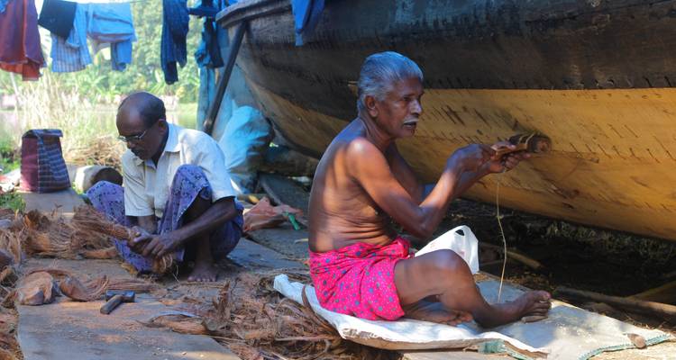Deux hommes assis travaillant sur des cordes ou des filets à côté d'un grand bateau.
