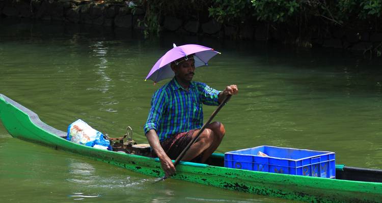 Homme qui pagaie dans un bateau vert avec un parasol sur une rivière.