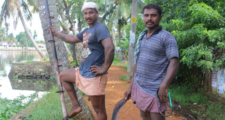 Deux hommes debout près d'un sentier bordé de palmiers et d'un plan d'eau.