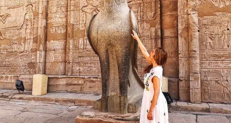 Vrouw in een jurk die een groot standbeeld aanraakt in een oude tempel.