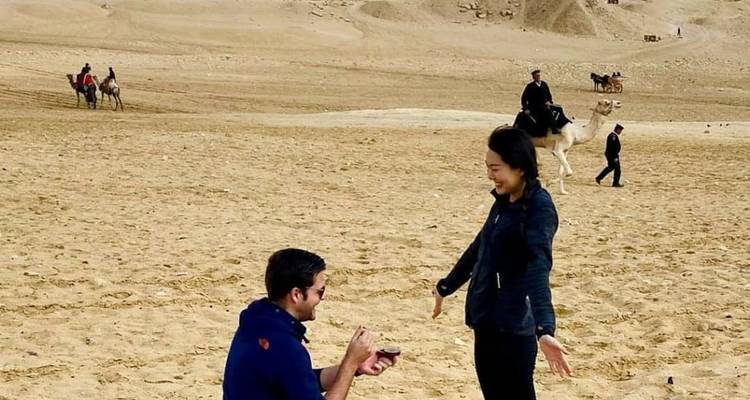 Ein Mann, der einer Frau in einer Wüste einen Heiratsantrag macht, mit Kamelen im Hintergrund.