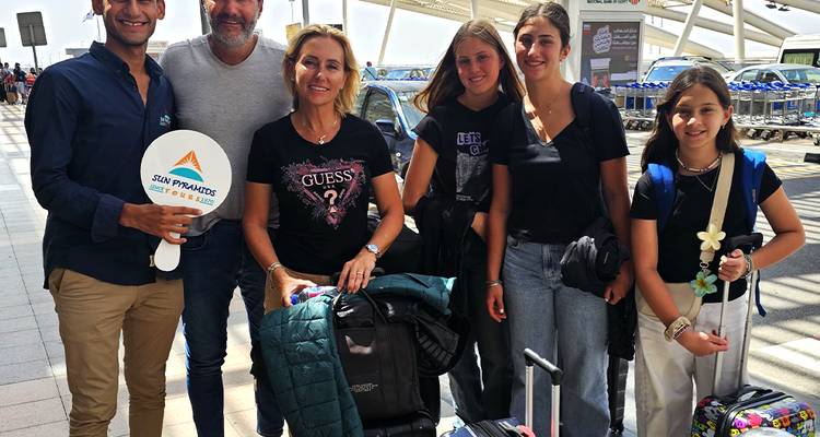 Family with luggage at an airport holding a sign.