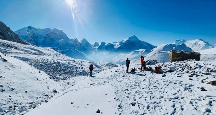 Trekker stehen in einem verschneiten Himalaya-Pass, umgeben von aufragenden weißen Gipfeln und strahlender Sonne.