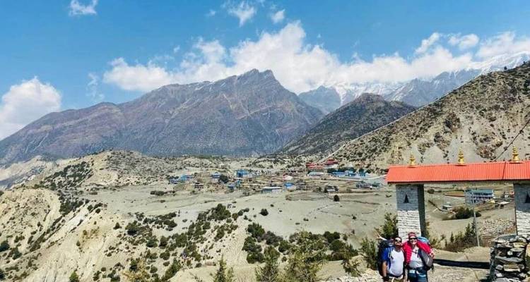 Blick über ein trockenes Bergtal zur Siedlung Muktinath mit Trekkern, die bei einer kleinen Stupa posieren.