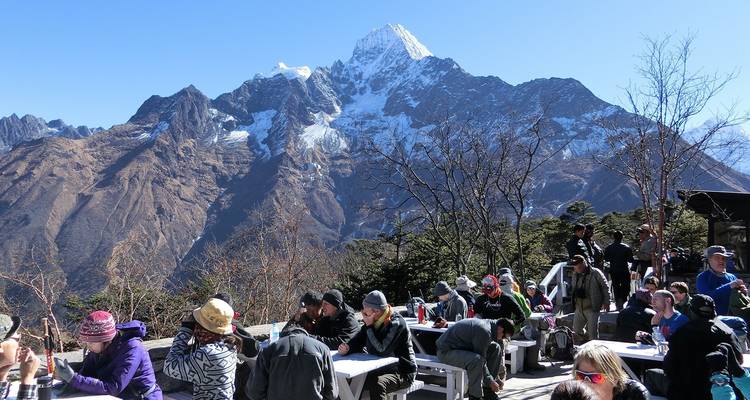 People dining outdoors with a stunning snowy mountain in the background.