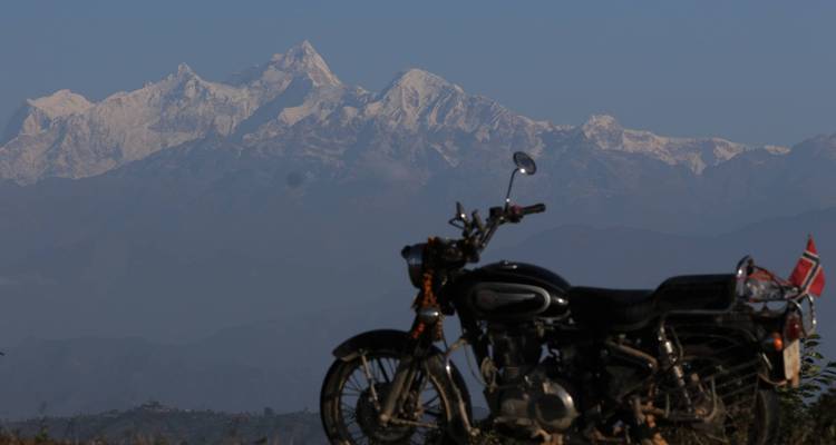 Motorfiets op de voorgrond met besneeuwde bergen op de achtergrond.