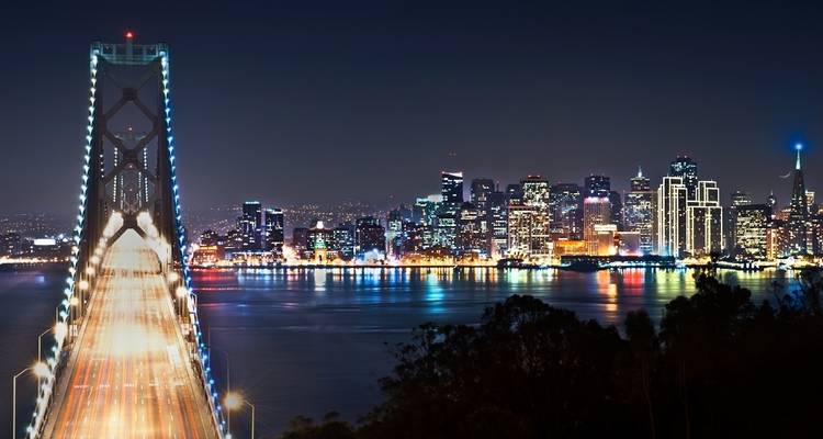 Night view of a bridge with city lights in the background.