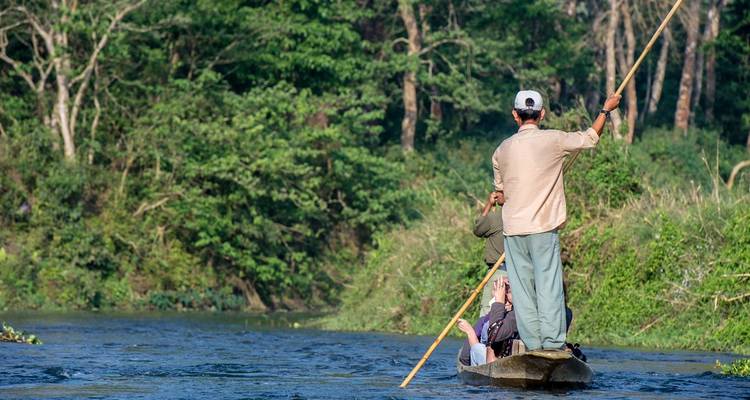 Two men on a wooden boat navigating through a river.