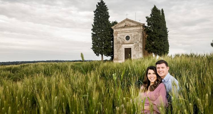 Couple assis dans un champ herbeux avec une chapelle derrière.