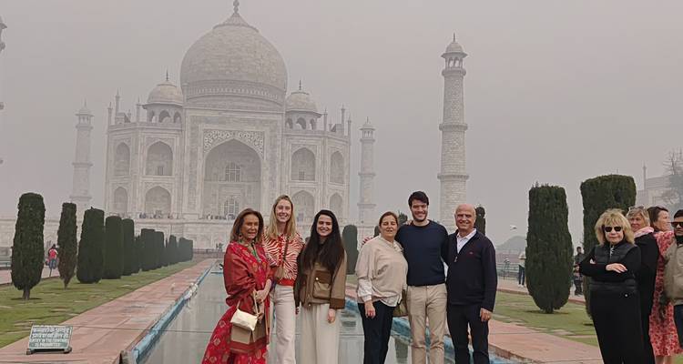 Un groupe de voyageurs pose devant le Taj Mahal enveloppé de brume, le long de son bassin de réflexion.