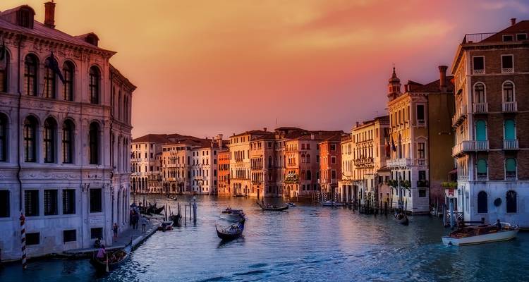 Les couleurs du coucher de soleil sur le Grand Canal de Venise avec des gondoles et des palais historiques bordant l'eau.
