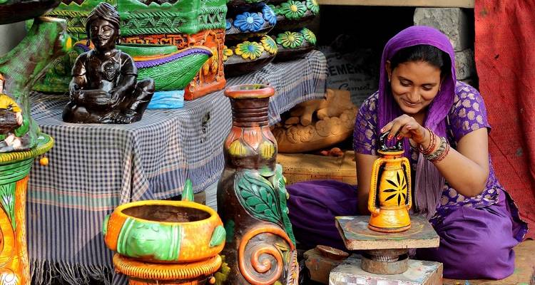 Une femme en vêtements traditionnels travaillant la poterie, entourée d'objets ménagers colorés.