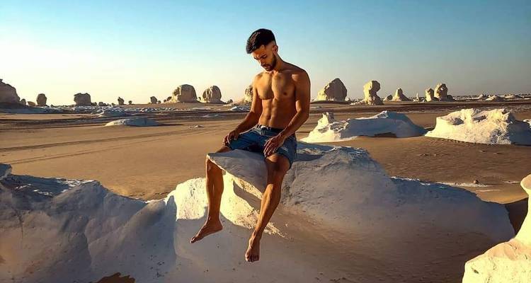 Een persoon die zit op witte rotsformaties in een woestijnomgeving.