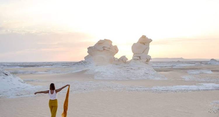 Een persoon met een sjaal die tijdens zonsondergang naar rotsformaties loopt.