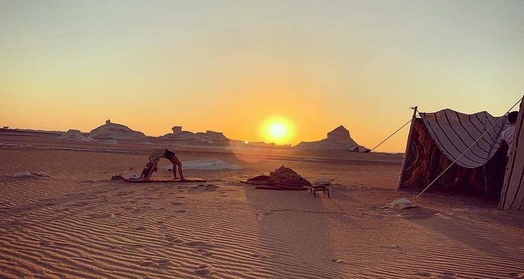 Zonsondergangzicht over een woestijnlandschap met tenten en een persoon die yoga beoefent.