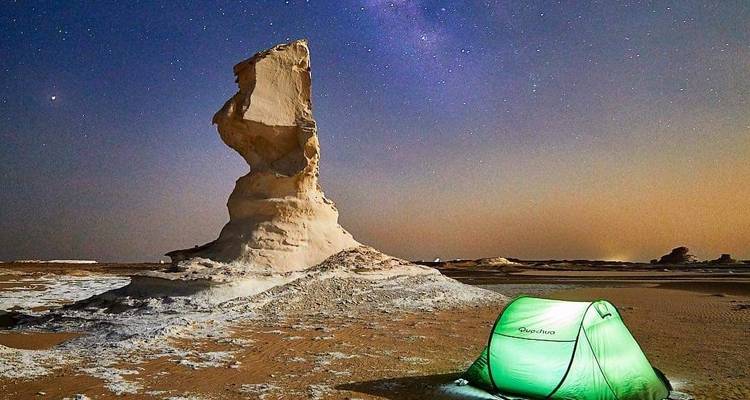 Une formation rocheuse blanche sous un ciel étoilé avec une tente verte au premier plan.