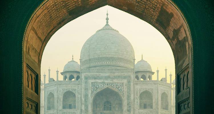 Iconic view of the Taj Mahal framed by a dark Mughal arch at soft dawn light.