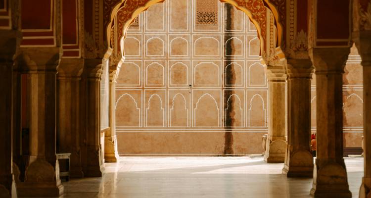 Elegant sandstone arcade with ornate arches and patterned walls inside an Indian palace in Jaipur.