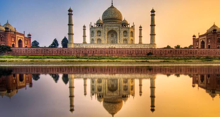 Taj Mahal reflected symmetrically in calm river waters at sunrise with pastel sky.