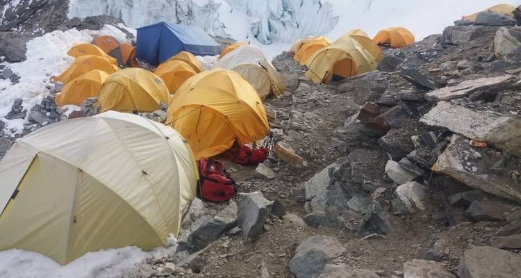 Groep kleurrijke tenten op een rotsachtige bergwand nabij een gletsjer.