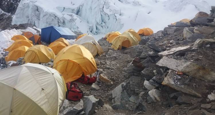 Basiskamp met gele tenten opgesteld op rotsachtig terrein nabij sneeuw.