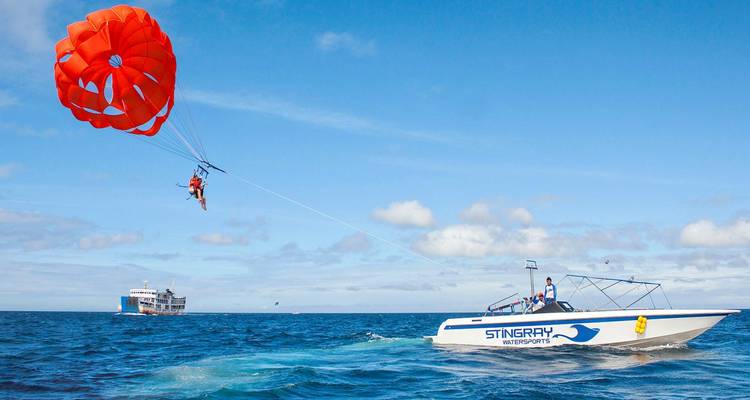 Parachute ascensionnel au-dessus de l'océan tiré par un hors-bord sous un ciel bleu éclatant