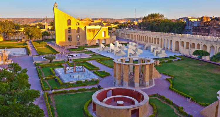 Vista general de los instrumentos del observatorio Jantar Mantar de Jaipur enmarcados por jardines cuidados al atardecer