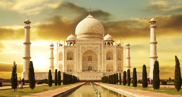 Lueur du lever de soleil sur le Taj Mahal avec reflet dans le bassin central et cyprès bordant le chemin