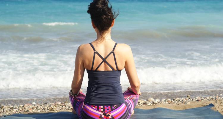 Jeune femme pratiquant la méditation assise sur un tapis de plage face aux vagues turquoise