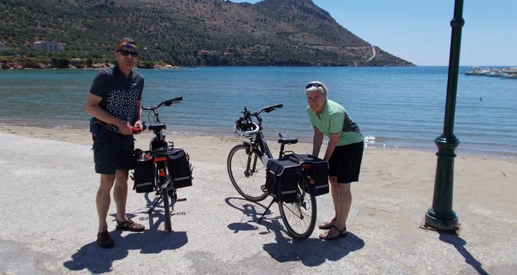 Deux individus avec des vélos près d'une plage avec des montagnes en arrière-plan.