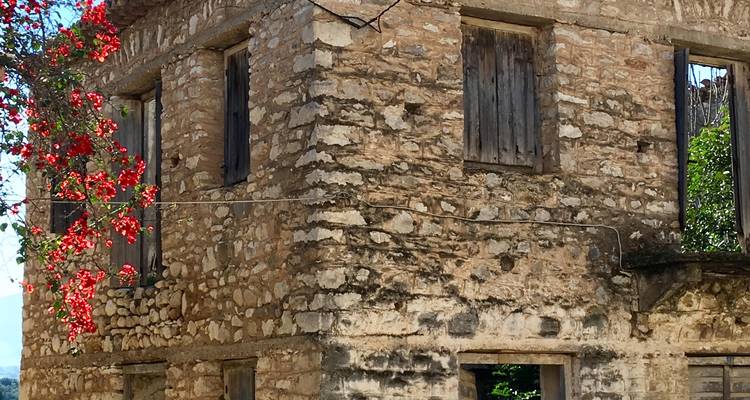 Ancien bâtiment en pierre avec de la verdure et des fleurs tout autour.