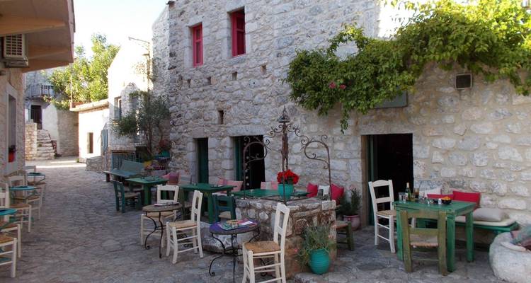 Charmante rue de village en pierre avec des tables et chaises colorées.