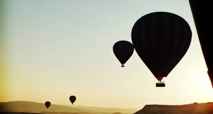 Silhouette von Heißluftballons bei Sonnenuntergang über einer Landschaft.